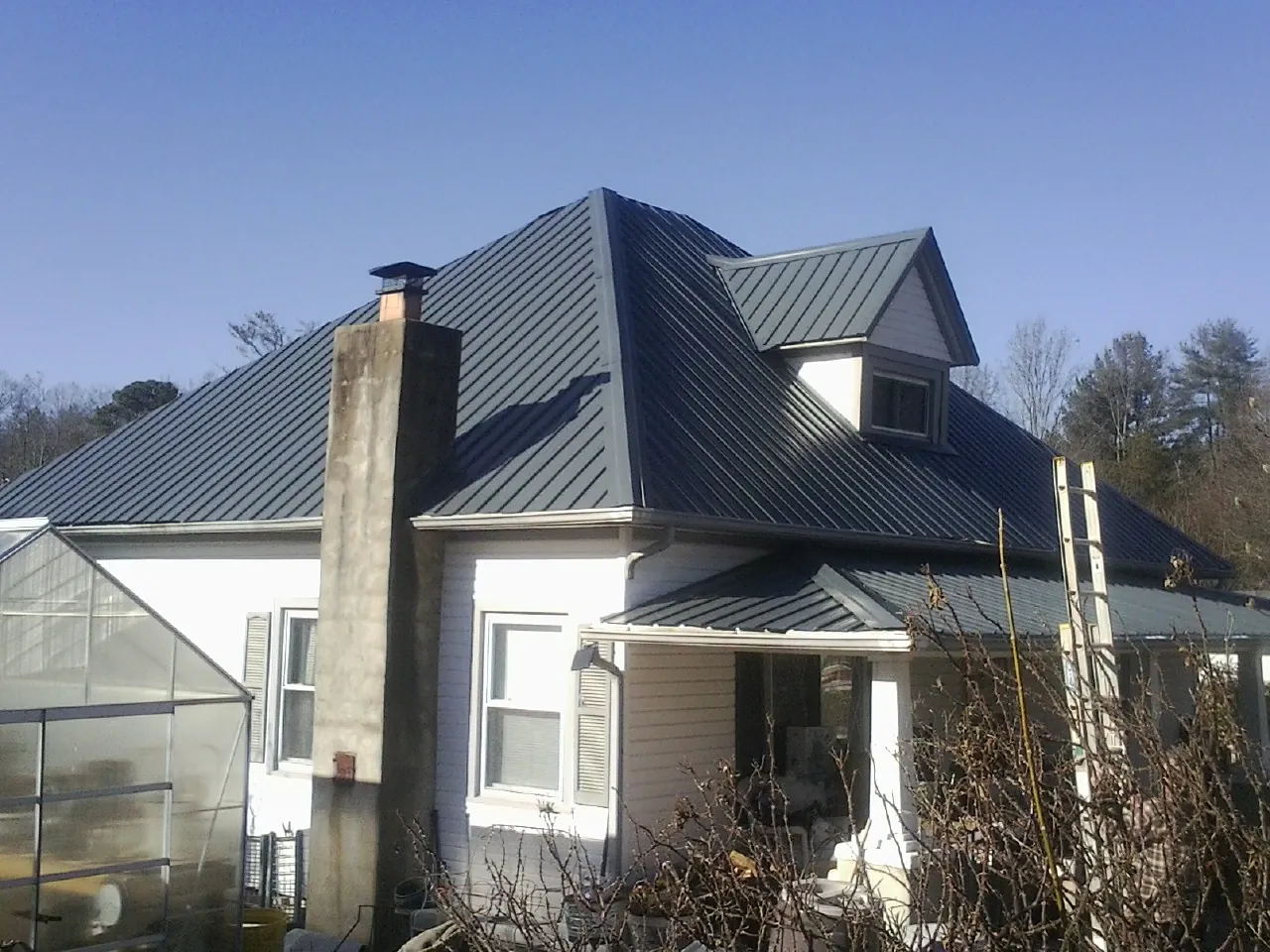 Dark blue standing seam metal roof on a white farmhouse with dormer — Slate & Tile Roof Repair by Roofing Brothers in Springer