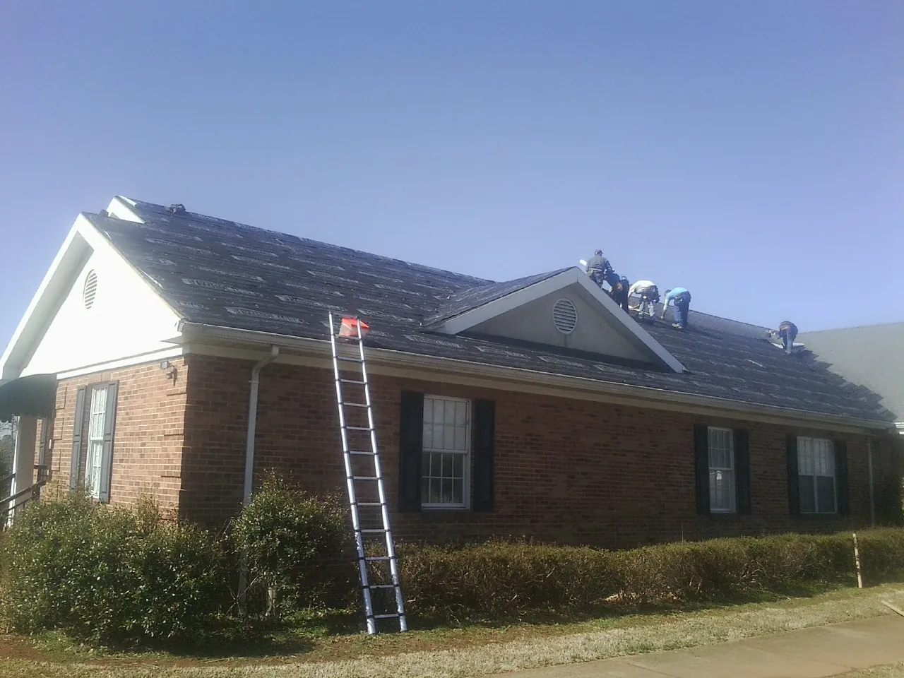 Crew tearing shingles off a brick ranch roof with a ladder set — Metal Roof Repair work by our crew in Springer