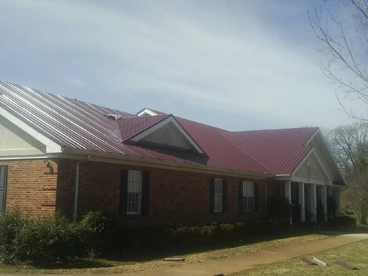 Red metal roof with gabled entries on a long brick building, from a Hail Damage Roof Repair job in Springer