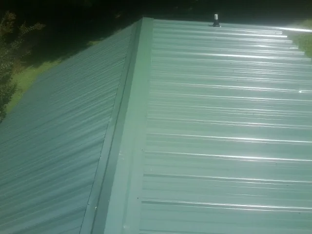 New green metal panels meeting at the ridge of a roof — Flat Roof Repair work by our crew in Springer