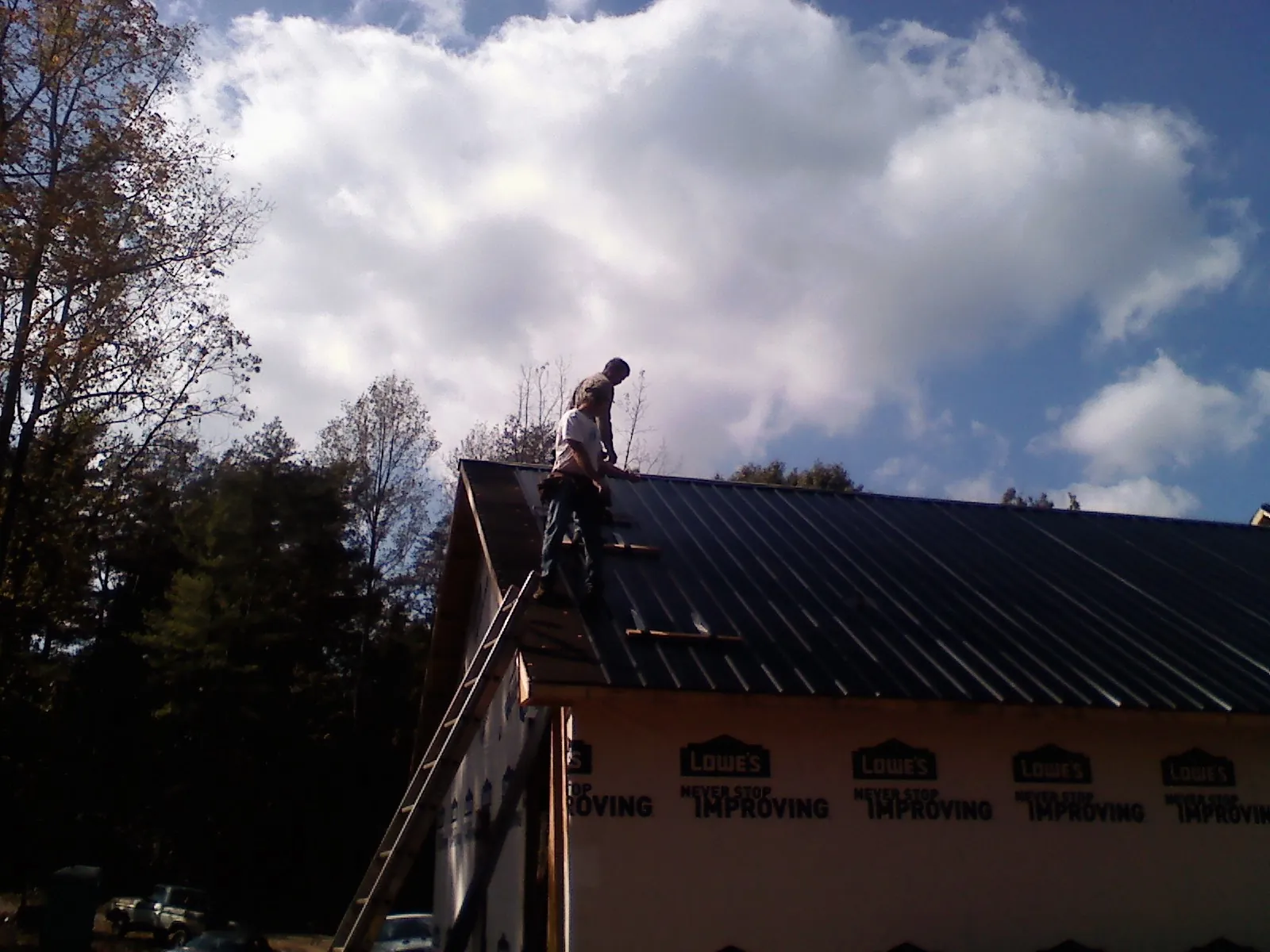 Roofer fastening dark metal panels high against a cloudy sky, from a Roof Inspection job in Springer