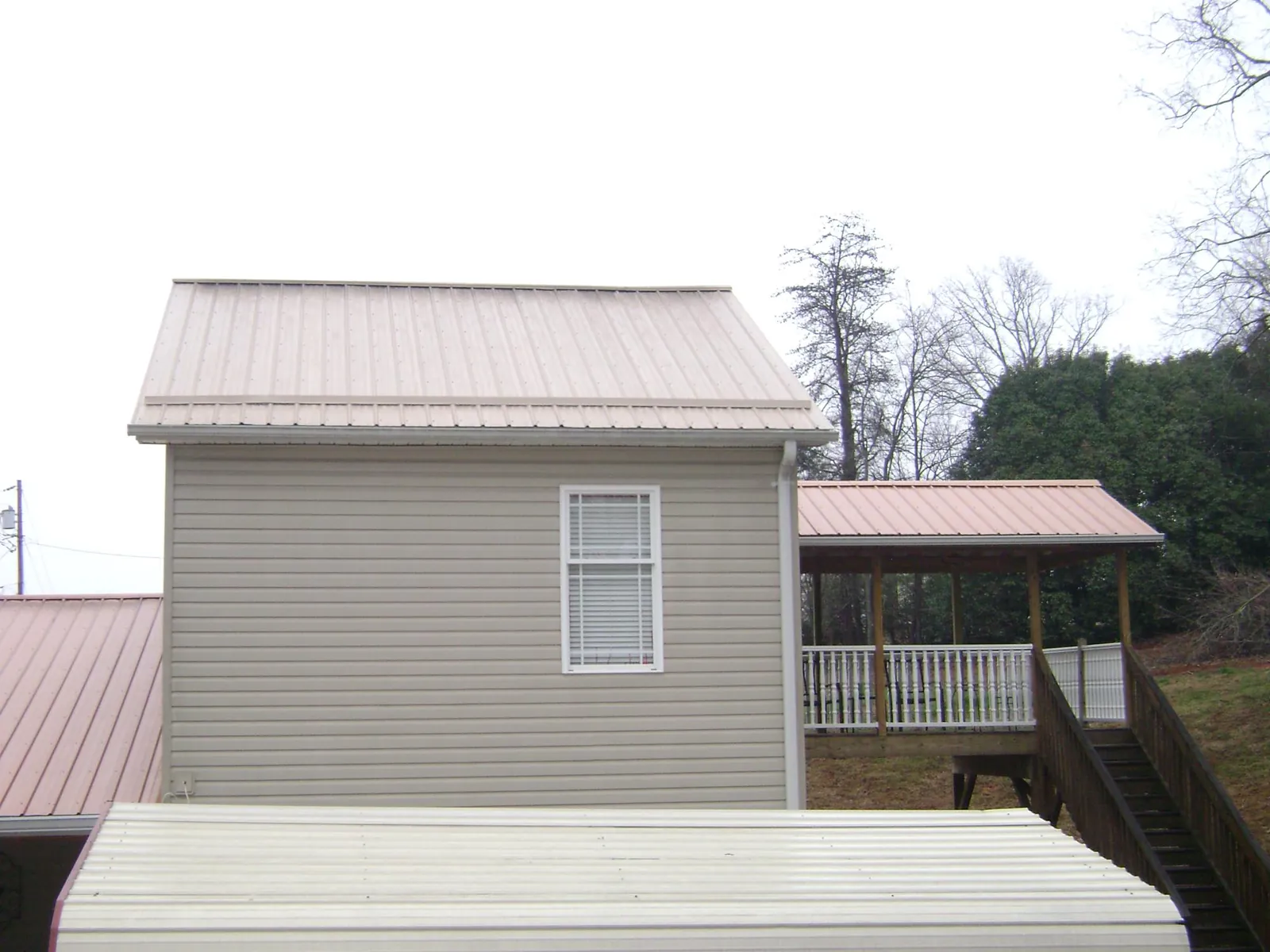 Tan metal roofs on a two story addition and attached porch, from a Roof Replacement job in Springer